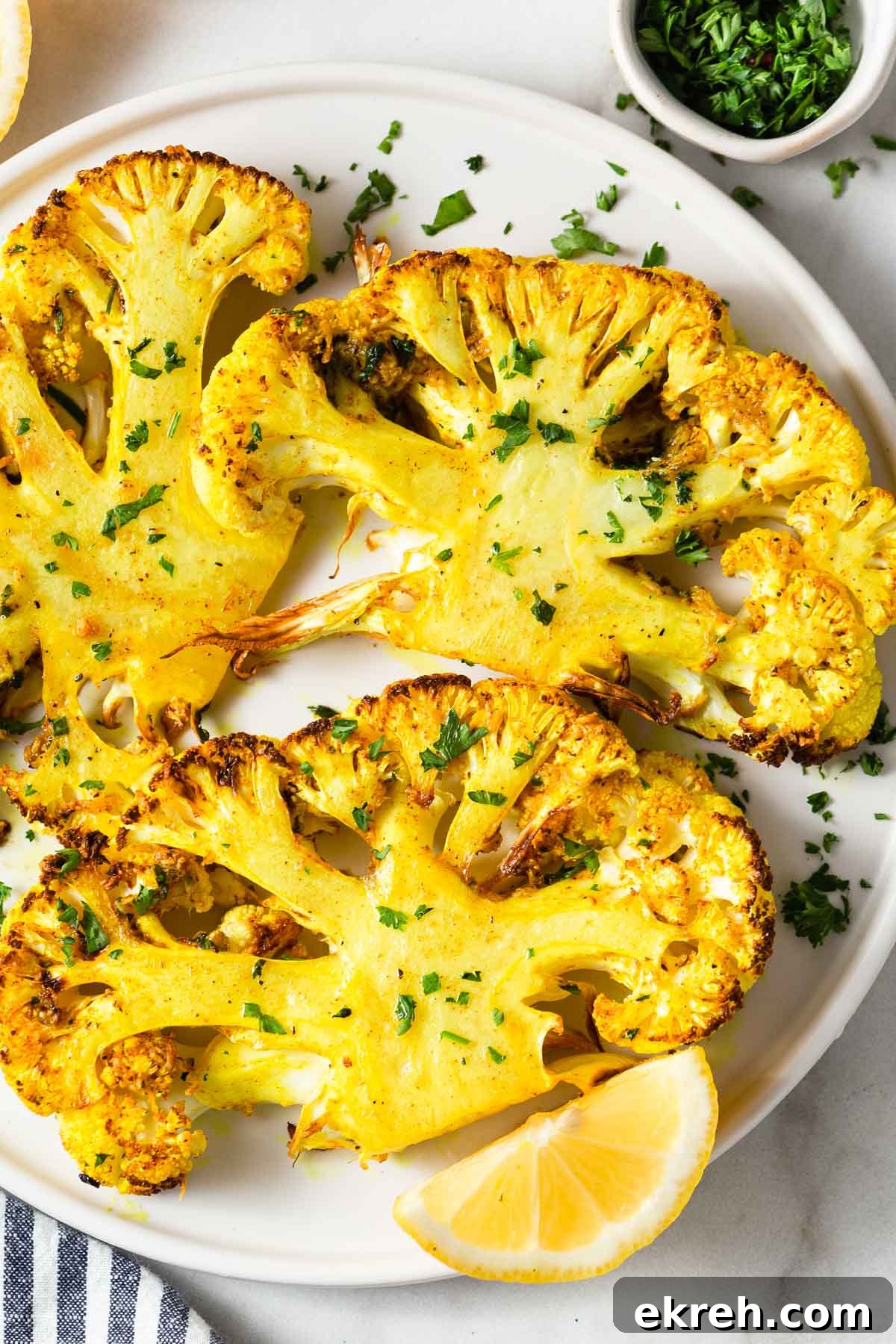 air fryer cauliflower steaks with parsley and lemon wedges on a plate.