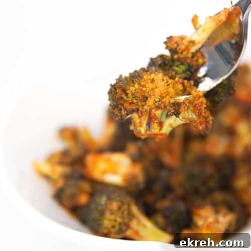 a white bowl of cooked broccoli with sriracha sauce on a fork