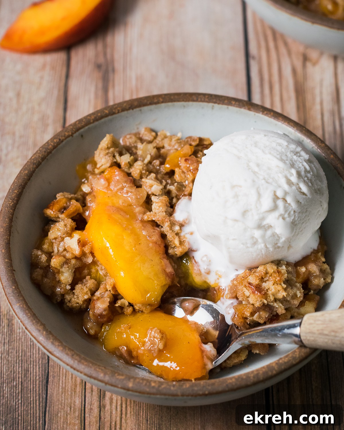 A bowl of gluten free peach crisp topped with vanilla ice cream.