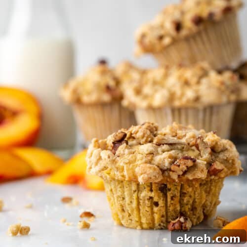 Gluten free peach muffins on a white table with a jar of milk.