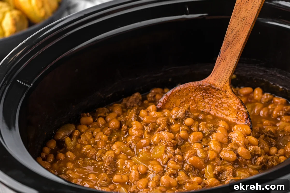 Pot of baked cowboy beans with a wooden spoon in them.