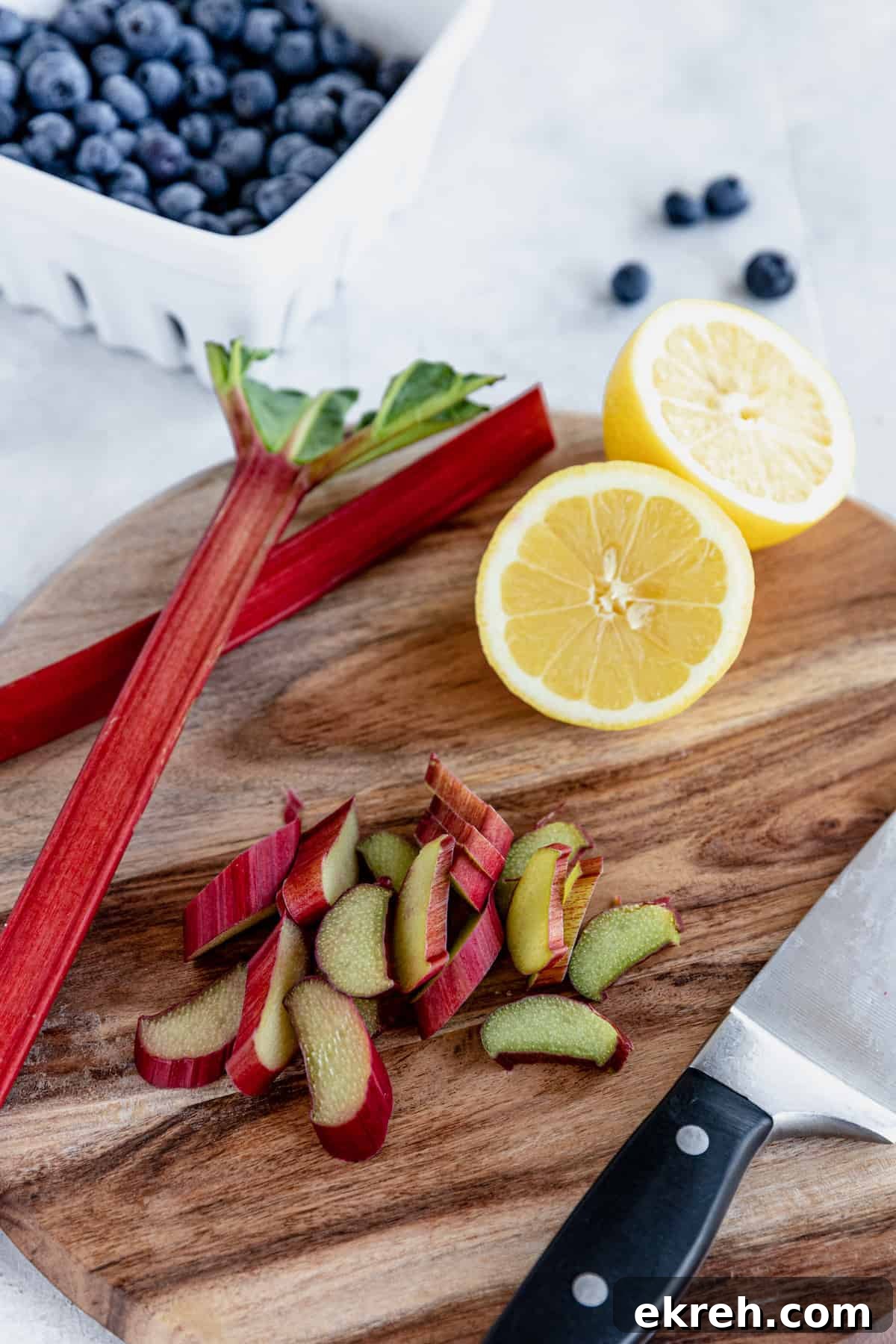 Chopped Rhubarb and a Halved Lemon on a Cutting Board with a Bowl of Blueberries in the Background