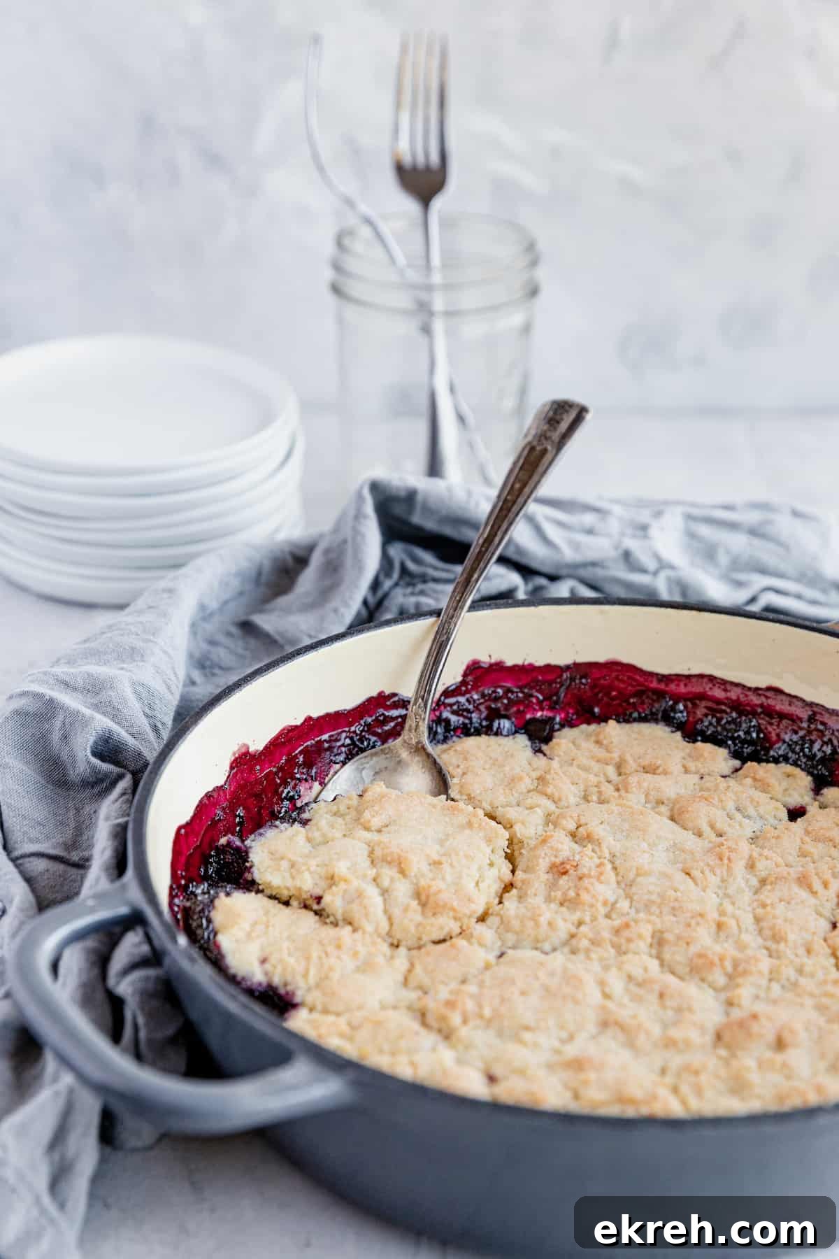 A Freshly Made Blueberry Rhubarb Cobbler in a Pan with a Metal Spoon Digging Into the Dessert