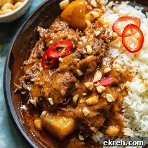Close up shot of short rib massaman curry in a plate on a bed of rice topped with peanuts and chilli slices