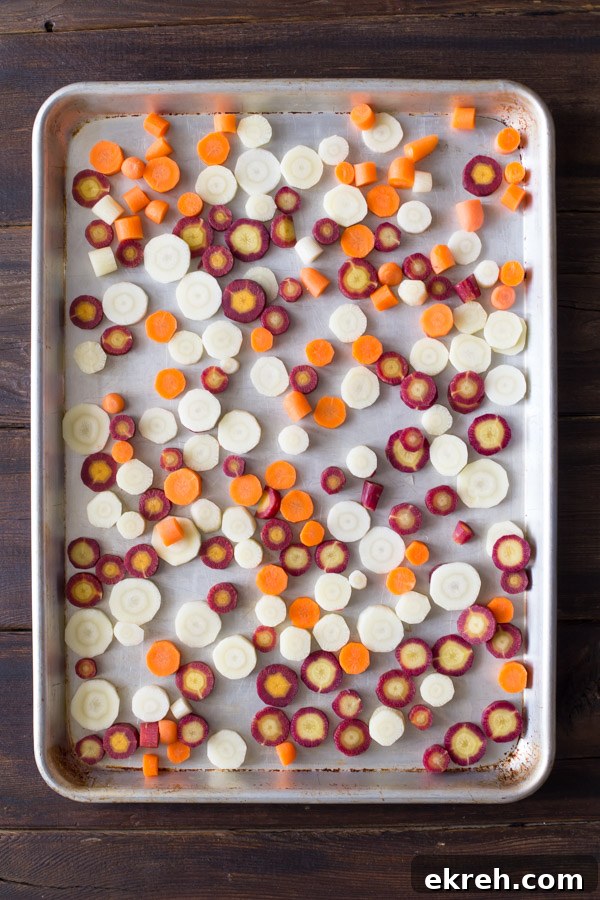 Purple, white and orange carrot slices on a baking sheet before roasting.