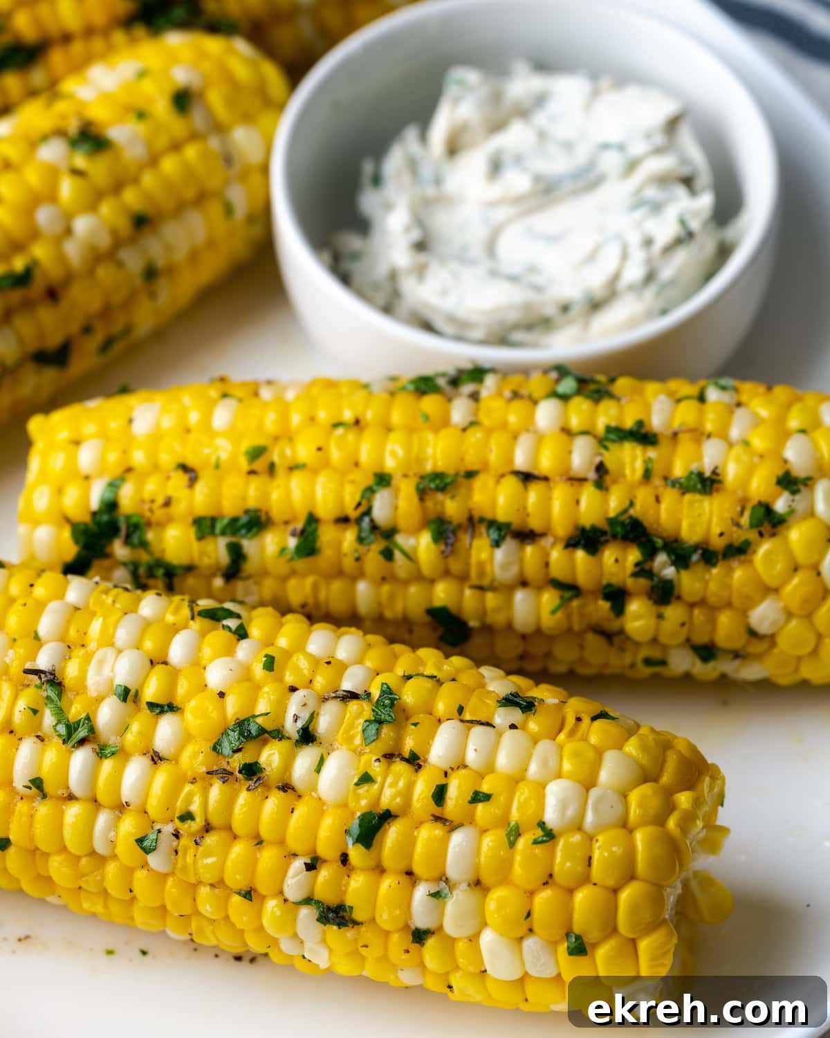 Corn on the cob coated with butter and herbs, next to a dish of herb butter.