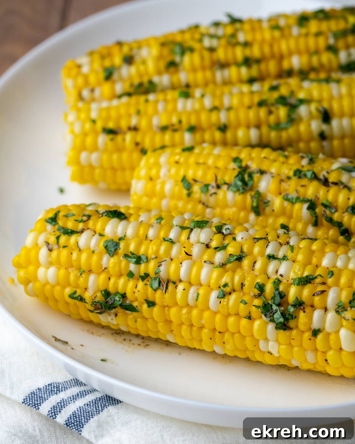Corn on the cob coated with herb butter on a white plate.
