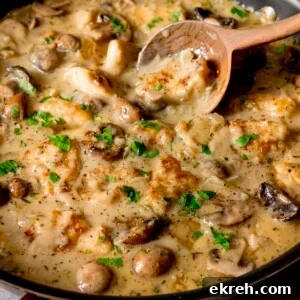 Square close-up image a large pan filled with creamy chicken and mushroom casserole. There is a wooden spoon in the pan.