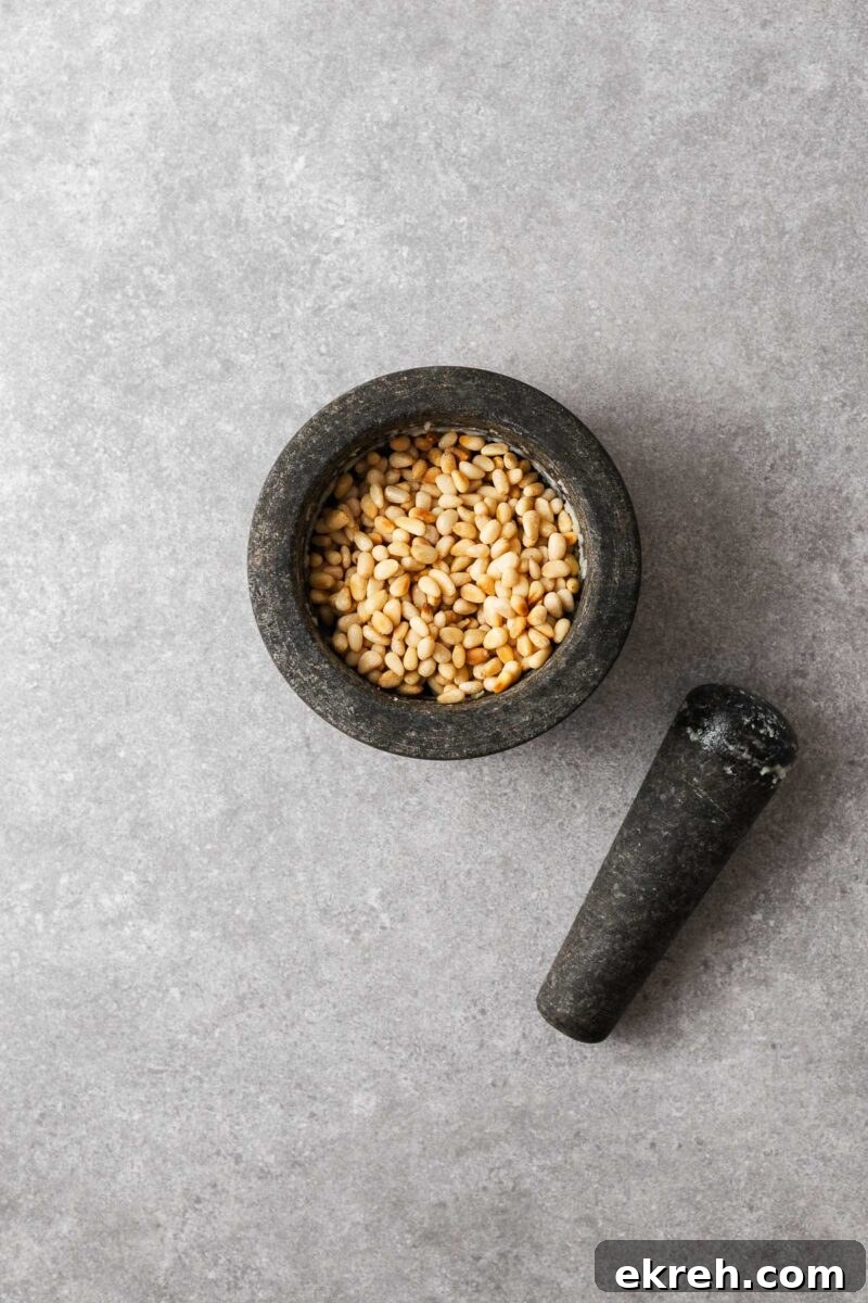 Toasted pine nuts in a mortar with pestle on the side.