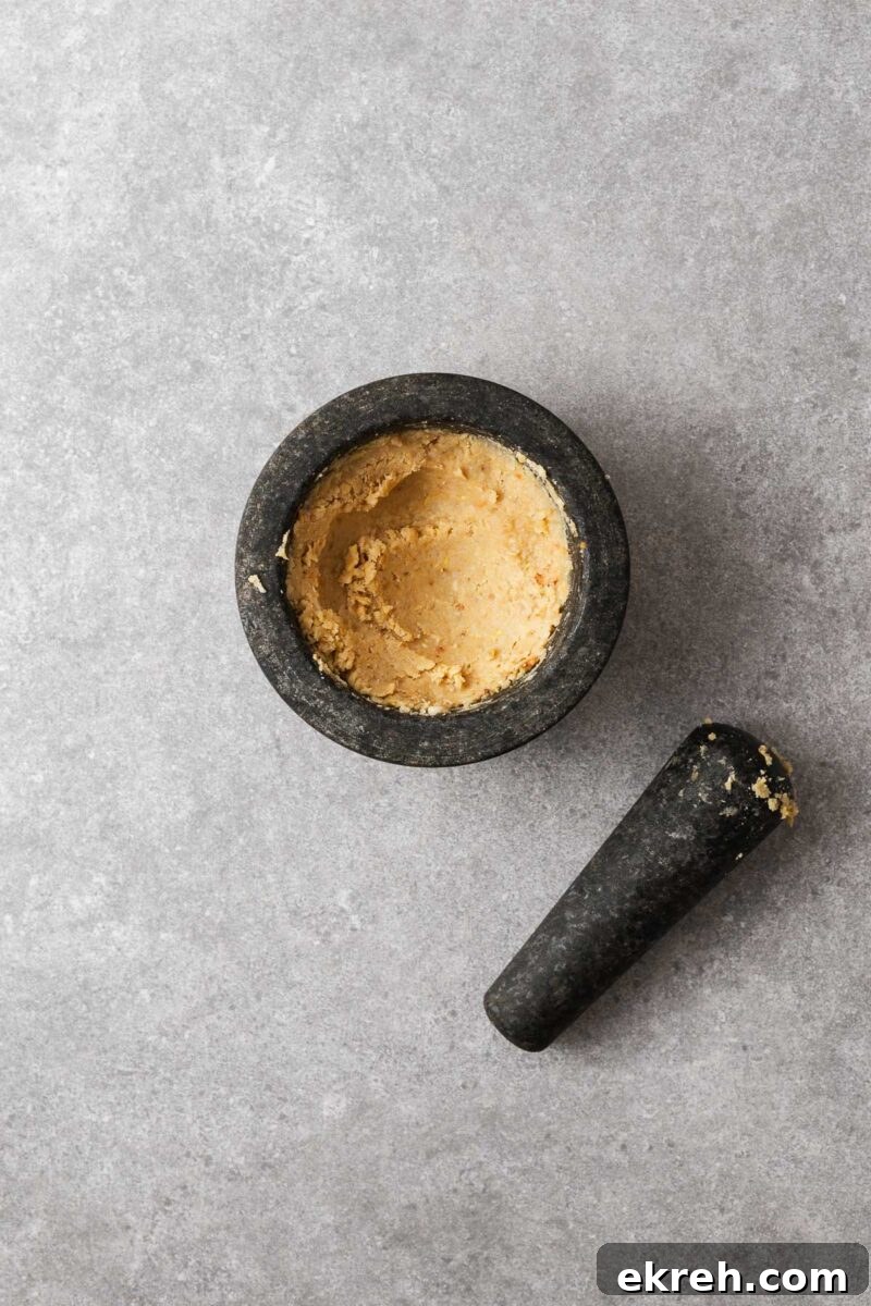 Toasted pine nuts in a mortar pounded with a pestle into a pine nut paste.