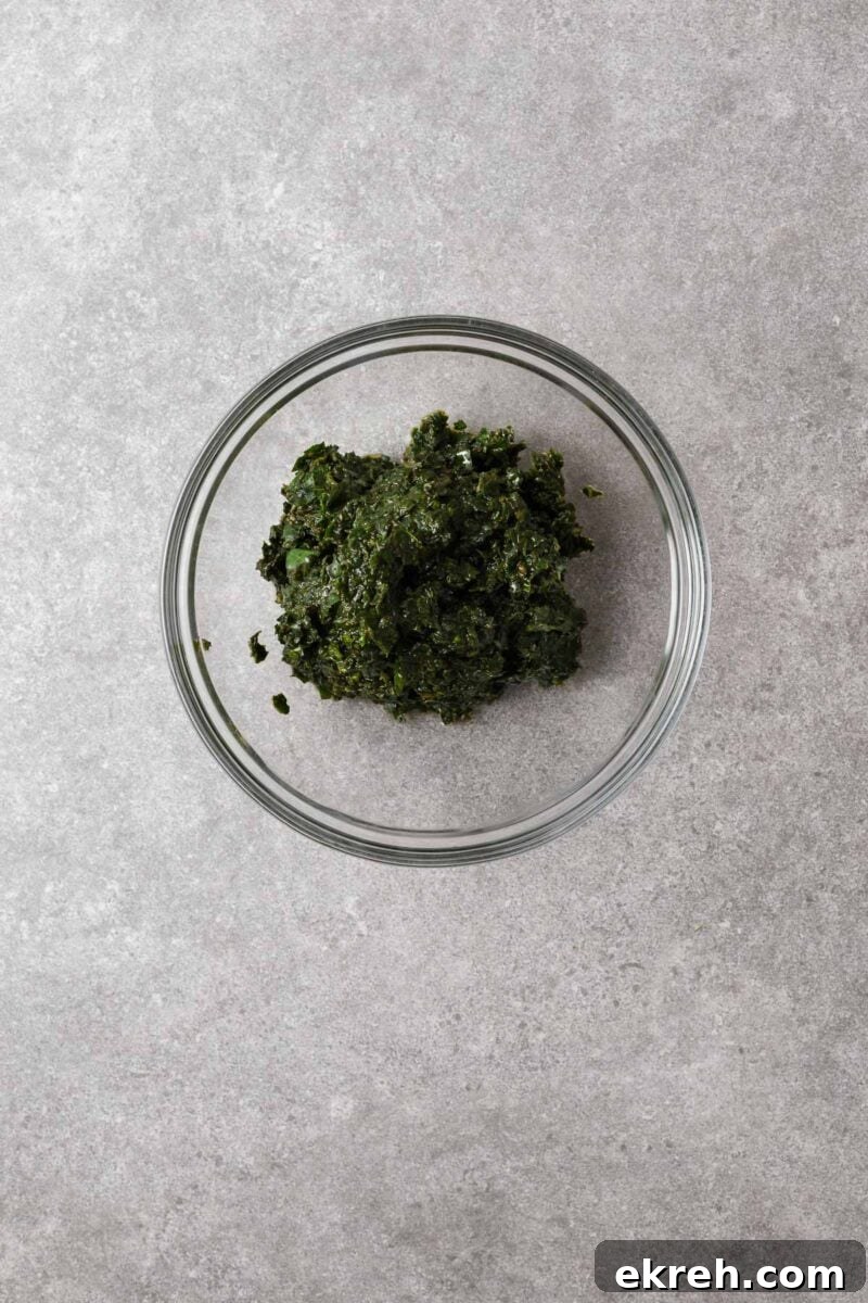 A glass mixing bowl with basil paste made by blending fresh basil leaves in a food processor.