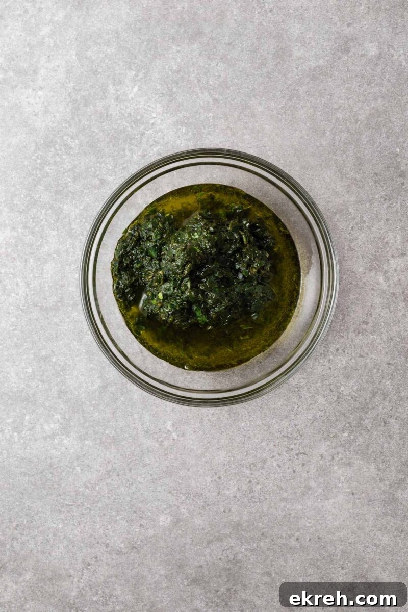 A glass mixing bowl with food processor basil paste and olive oil.