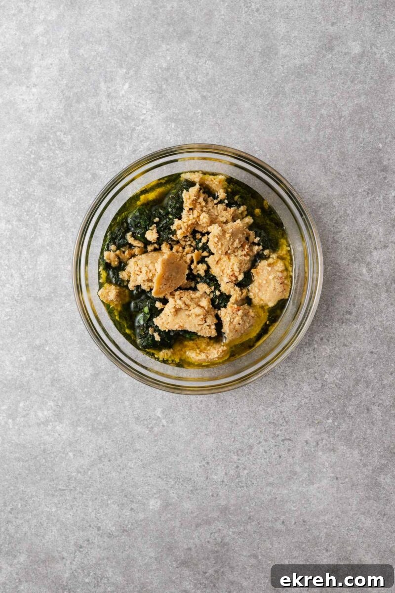 A glass mixing bowl with basil paste and pine nut paste for making pesto.