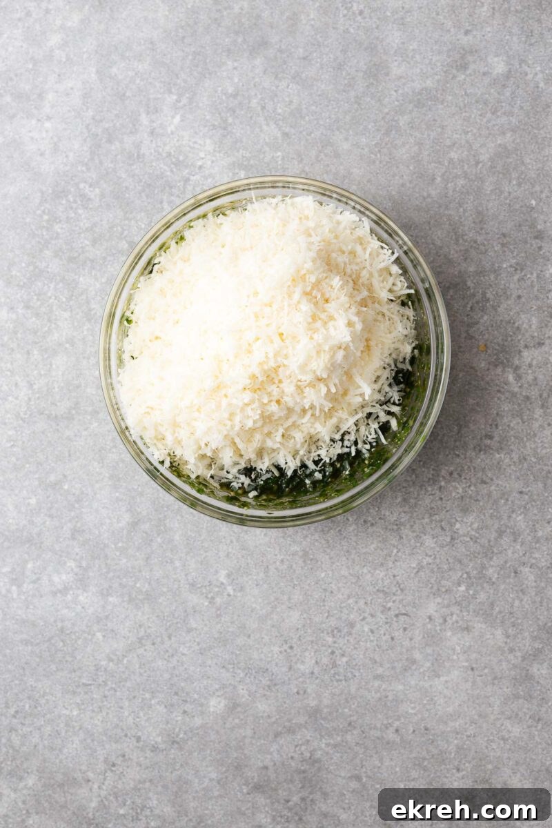 Freshly grated parmesan cheese added to a bowl of basil and pine nut paste to make basil pesto.