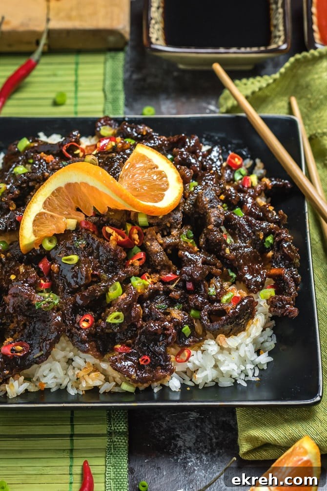 Plated orange beef served over rice with garnishes.