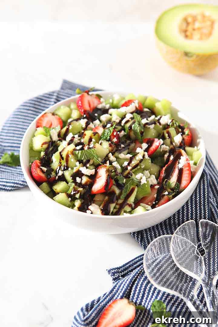 A Strawberry Melon Salad is shown in a bowl with tongs, ready for serving