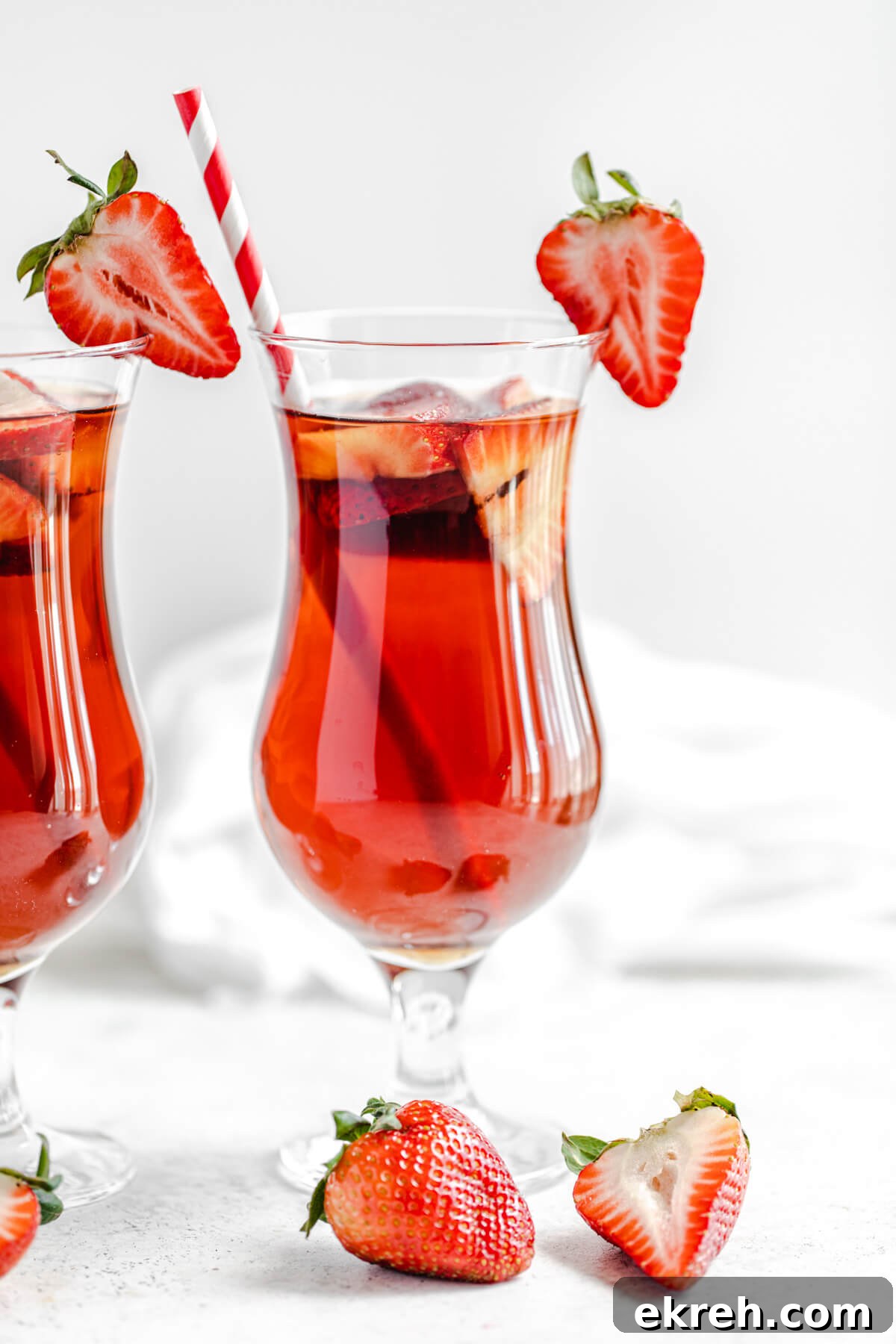 Homemade Strawberry Iced Tea Recipe 8 close up of glass of iced tea with halved strawberry on the rim of the glass and a red striped paper straw inside