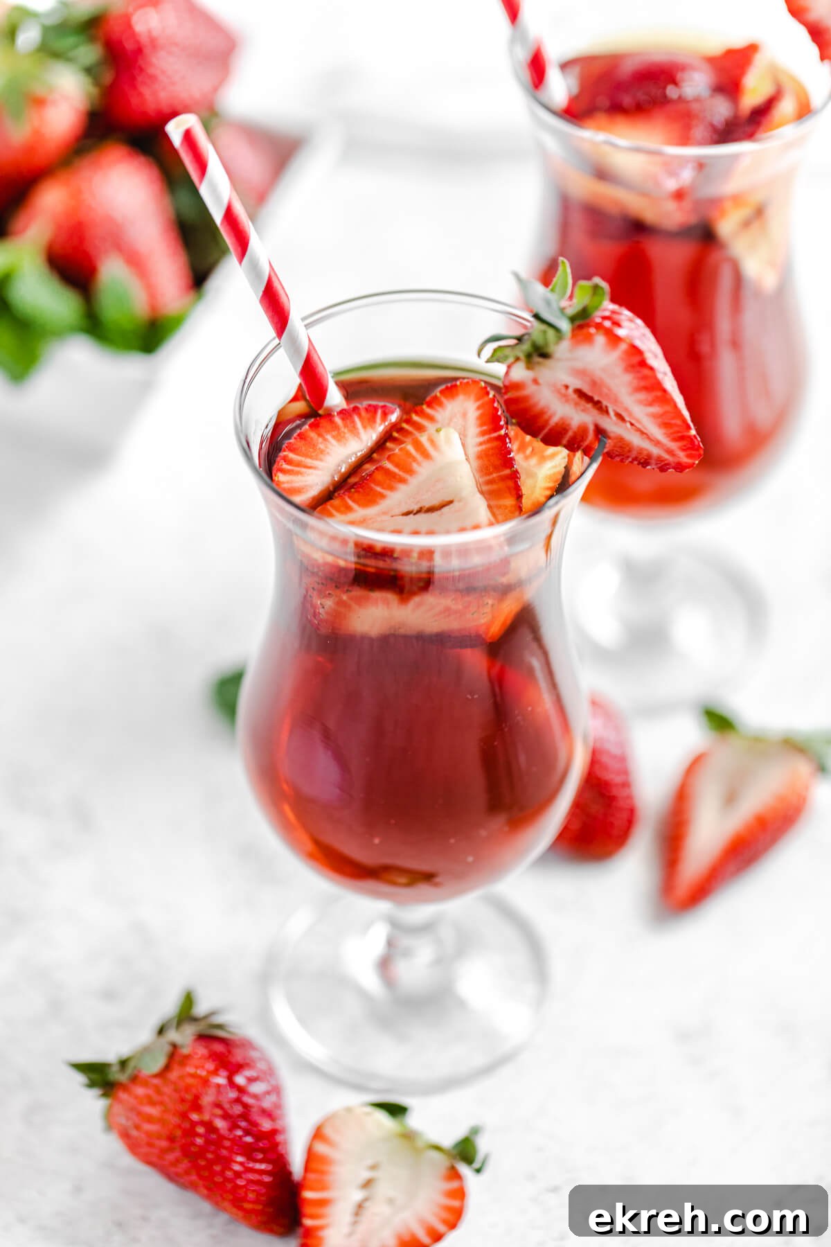 Homemade Strawberry Iced Tea Recipe 3 top angled view to show inside of glass with iced tea, fresh strawberries and a red striped paper straw inside