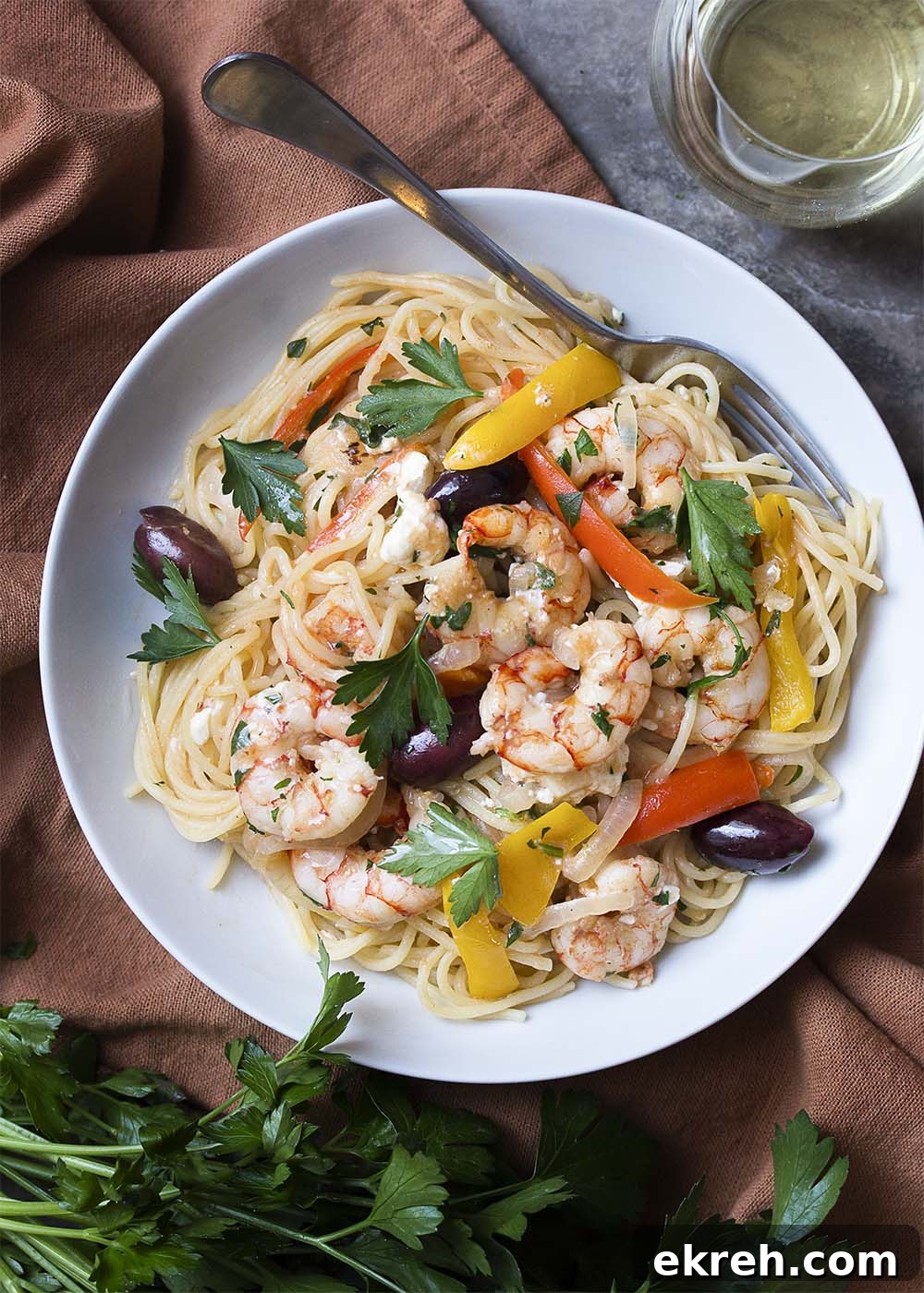 Top view of a white plate full of pasta topped with shrimp, olives, feta, and bell peppers.