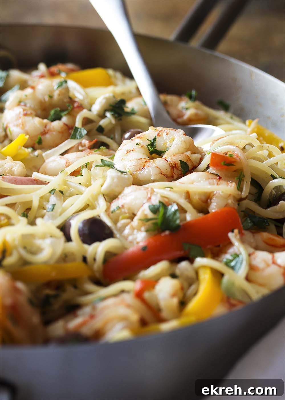 Close-up of a spoon serving a portion of shrimp and pasta from a large saute pan.
