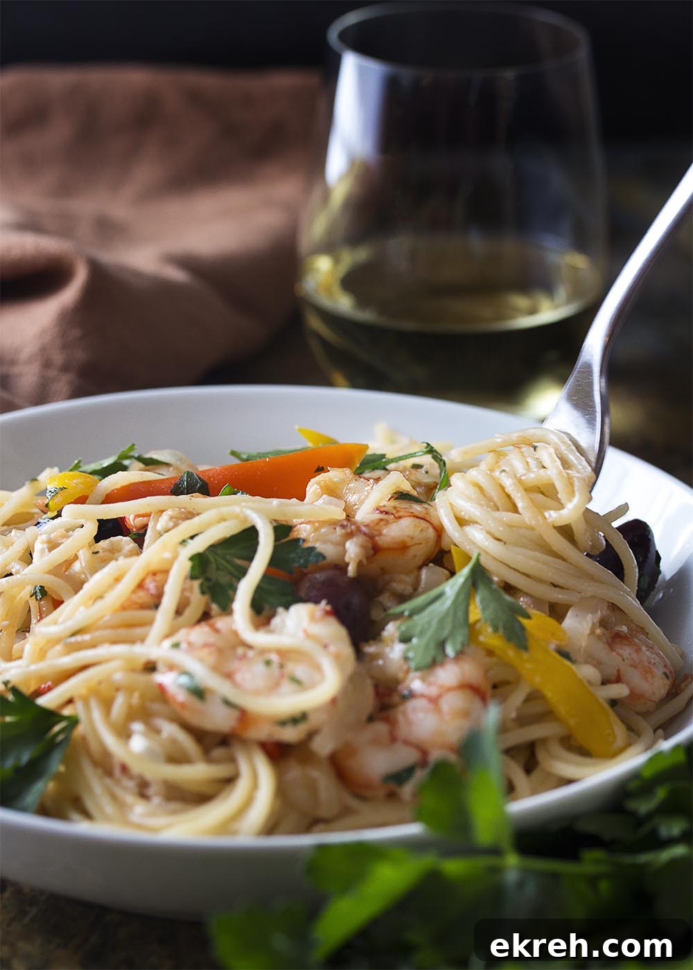 A fork twirling pasta in a white bowl full of Greek shrimp with pasta.