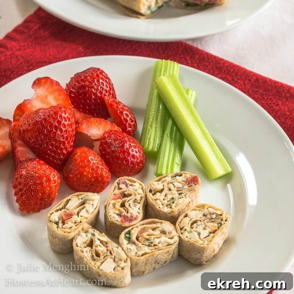 A plate of pinwheels made with sliced chicken and vegetable wrap. Strawberries and stalks of celery sit next to the pinwheels.