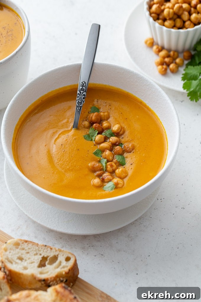 Creamy Roasted Sweet Potato and Carrot Soup Recipe 2 Up close view of sweet potato carrot soup in a white bowl and garnished with crispy chickpeas and chopped cilantro.