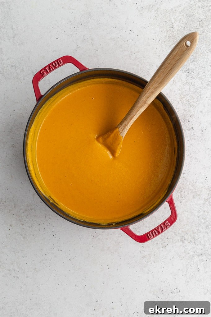 Creamy Roasted Sweet Potato and Carrot Soup Recipe 6 Overhead view of roasted sweet potato soup with coconut milk in a red pot with a wooden spoon inserted into it.