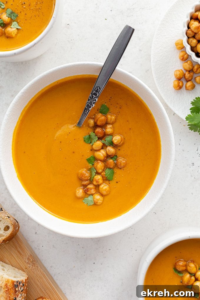 Creamy Roasted Sweet Potato and Carrot Soup Recipe 7 Overhead view of sweet potato and carrot soup in a white bowl with a spoon inserted into it.